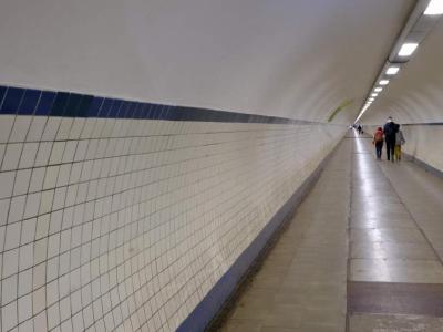 This is the foot tunnel that runs beneath the Scheldt river in Antwerp, Belgium. Tiled pedestrian tunnel with people walking away in the distance.