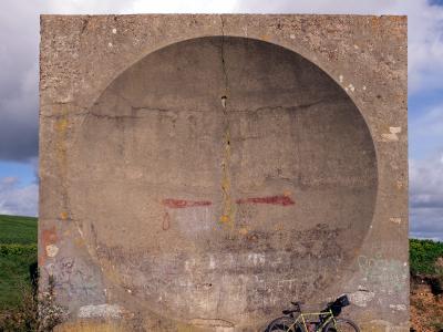 Concrete acoustic mirror with a bicycle leaning against it in a rural field.