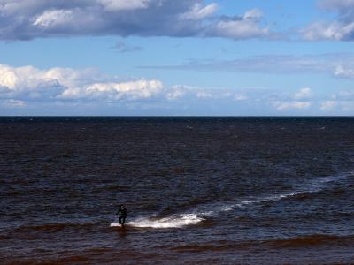 Kitesurfer gliding across choppy sea under a bright, cloudy sky.