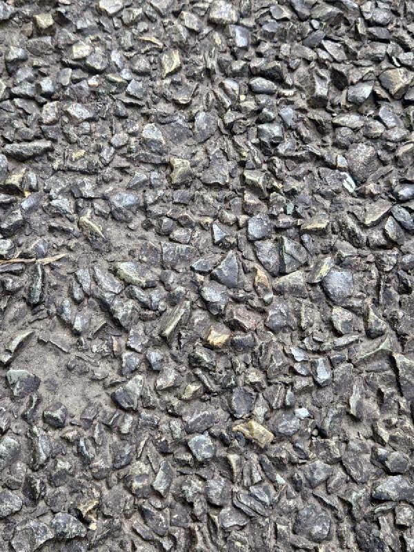 Textured surface of worn tarmac with exposed stone chippings embedded in grey bitumen, typical of aged rural road surfacing.